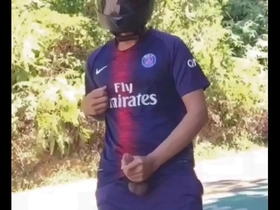 A biker in a football uniform masturbates outdoors in public.